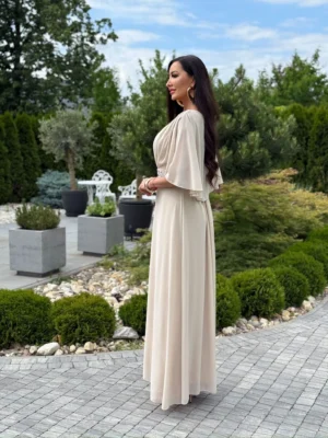 Beżowa sukienka maxi Aurelia na modelce – widok z boku na szeroki rękaw i długą, swobodnie opadającą spódnicę.