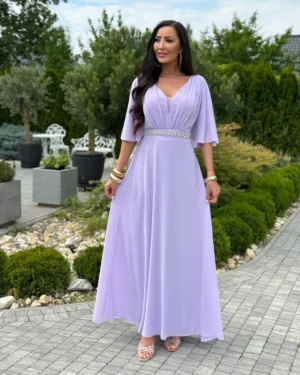 aurelia-fioletowa-sukienka-maxi-rozszerzany-dol Liliowa sukienka maxi Aurelia z ozdobną talią – modelka trzyma boki spódnicy, pokazując rozszerzany dół.